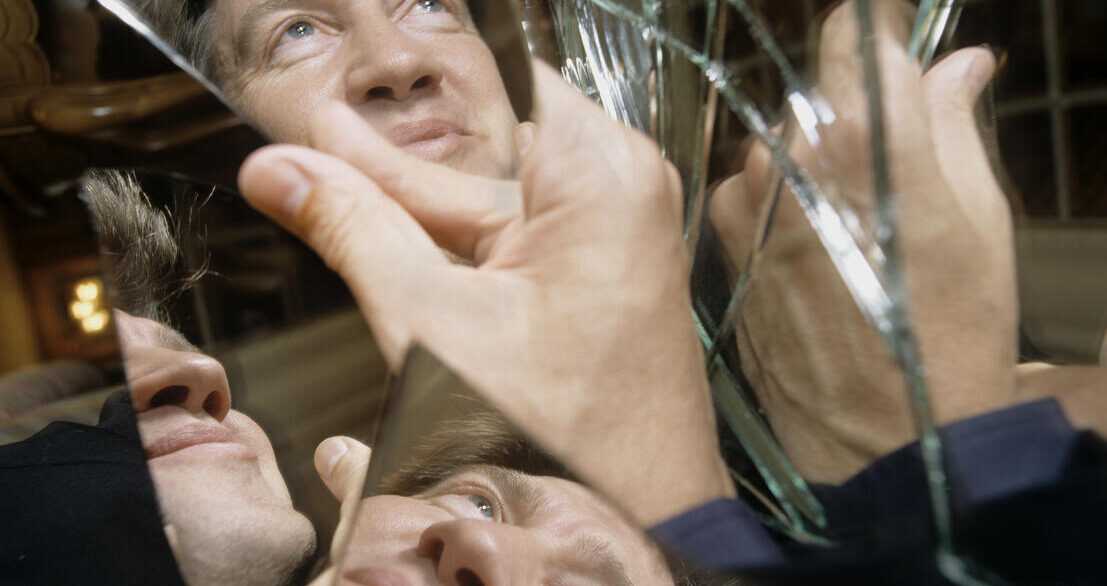 Film still from Lynch/Oz with David Lynch's face reflected in shards of broken mirror.