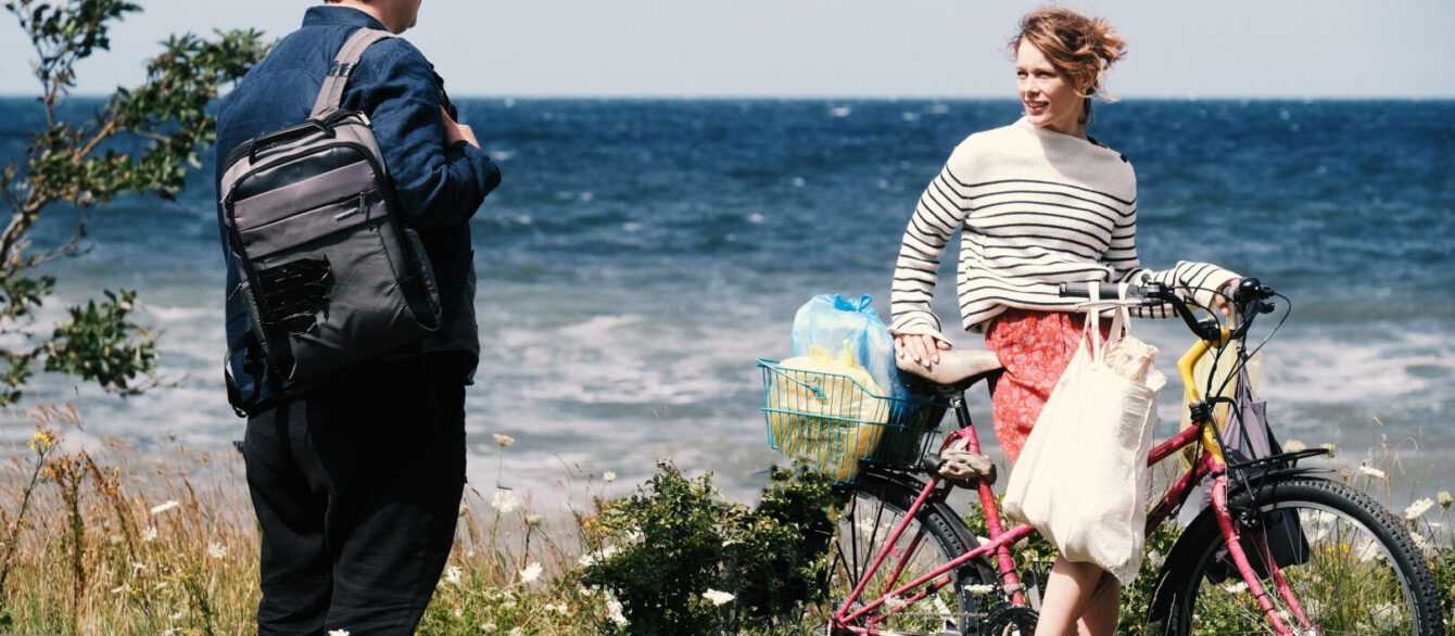 A film still from Afire with a woman in a bicycle talking to a man by the sea.