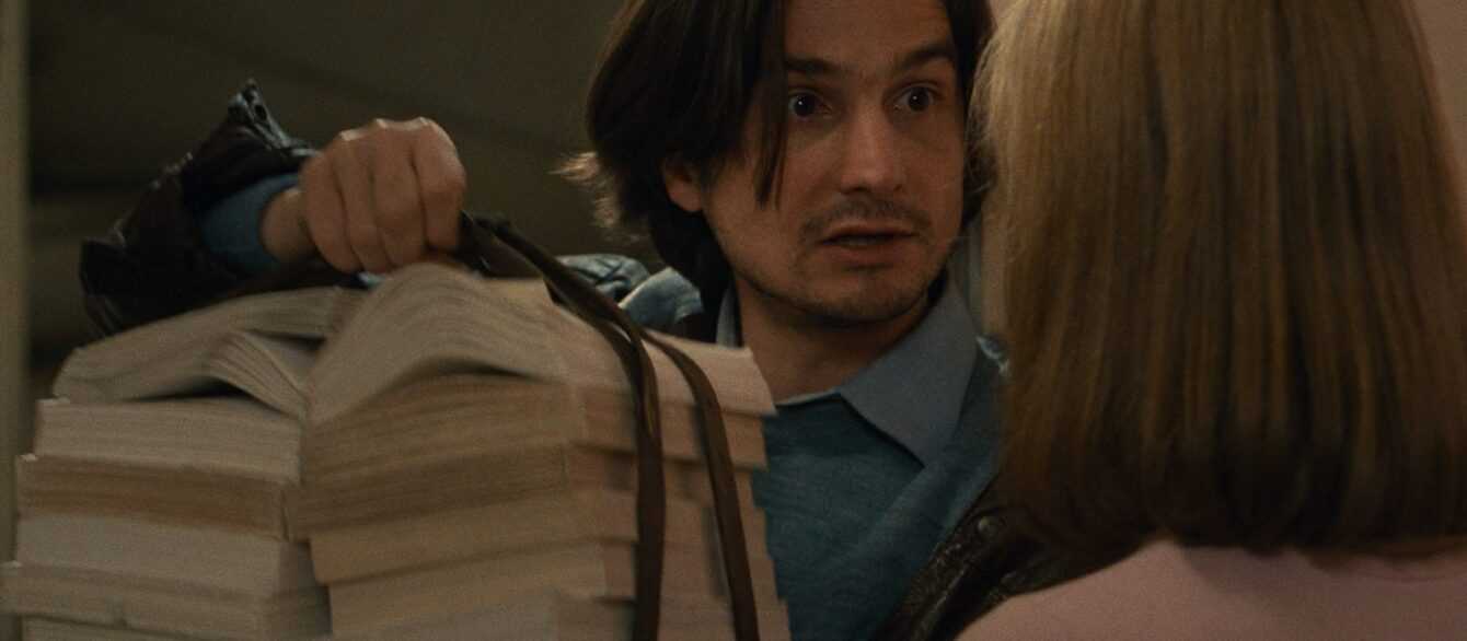 A film still from Love on the Run with Antoine Doinel holding a stack of books.