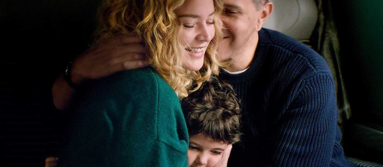 A film still from Other People's Children with Virginie Efira, Roschdy Zem, and Callie Ferreira-Goncalves laughing and embracing.