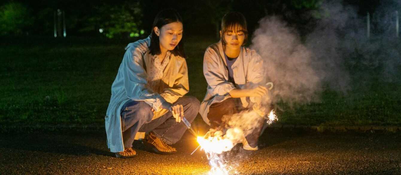 A film still from Remembering Every Night with two young women holding sparklers.