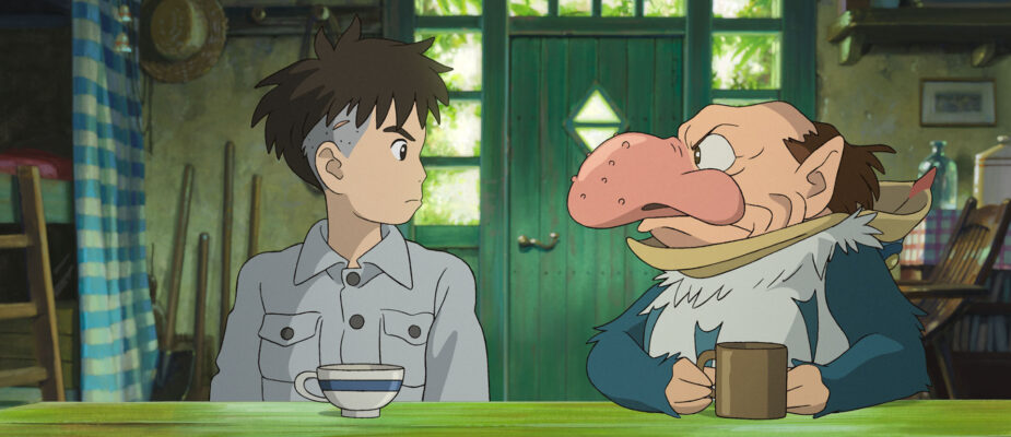 A film still from The Boy and the Heron. A boy and a squat, balding man with a large, beaked nose sit and look at each other tensely in a small cottage.